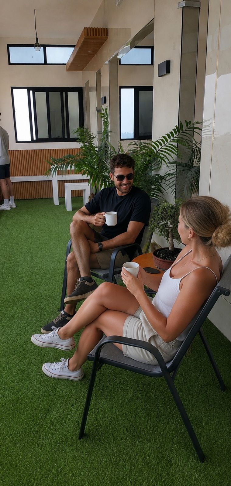 A modern outdoor seating area with artificial grass, metal chairs, and potted plants.