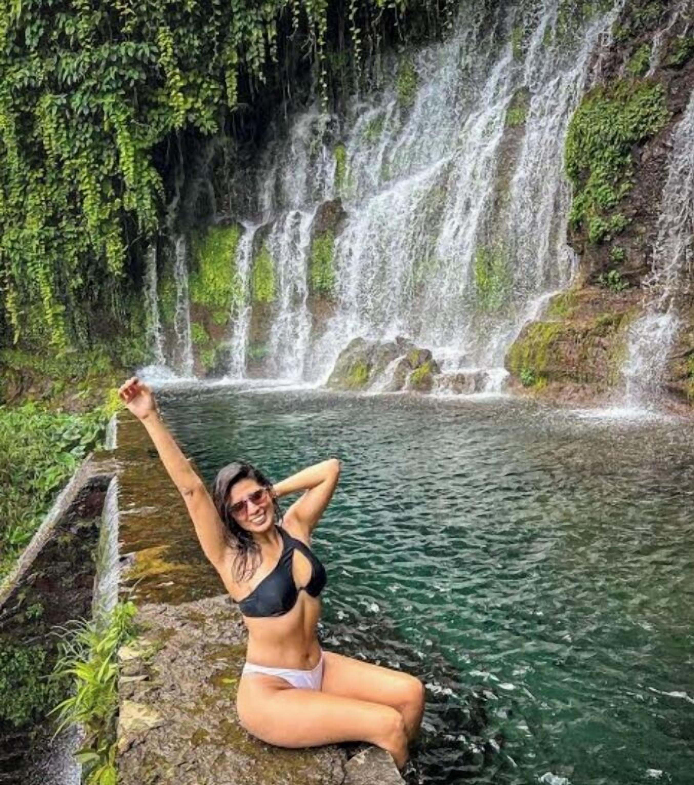 Una persona sentada junto a una cascada en un entorno natural.