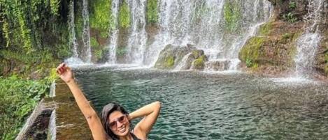 Una persona sentada junto a una cascada en un entorno natural.