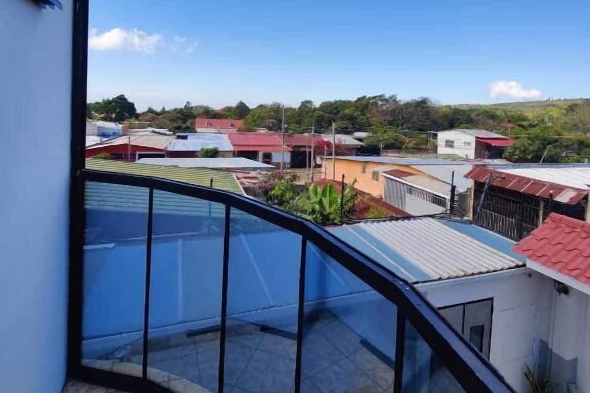 Un balcon offrant une vue dégagée sur un quartier résidentiel, avec des maisons aux toits rouges et un ciel bleu.