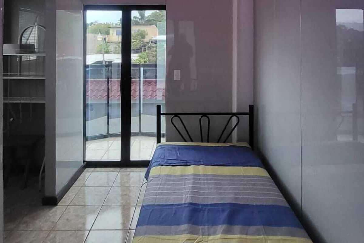Une chambre à coucher moderne avec un lit, un luminaire au plafond et une vue à travers une porte vitrée.