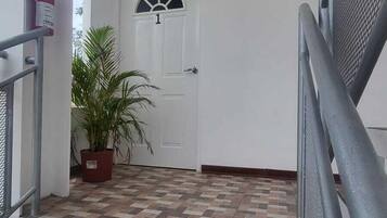 Una escalera lleva a una puerta con el número '1' encima, un extintor en la pared y una planta en maceta.