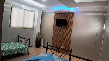 A bedroom with a bed, a small table, a potted plant, and a TV mounted on the wall.