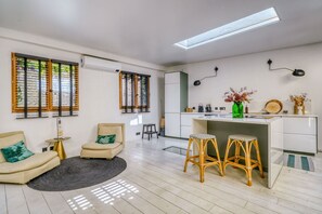 A modern living room with a sofa, chairs, a small round table, and a kitchen area with stools. - Chai Rooftop - Two Bedroom Apartment, Sleeps 4 (Bordeaux)