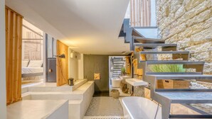 Een moderne badkamer met een badkuip, douche en een trap die naar een hoger gelegen verdieping leidt.