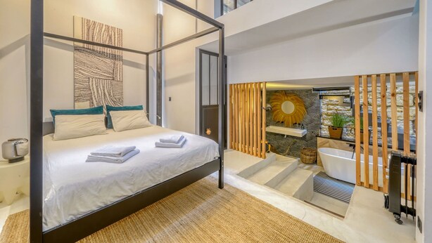 Een moderne slaapkamer met een hemelbed, een stenen muur, een badkuip en een groot raam.