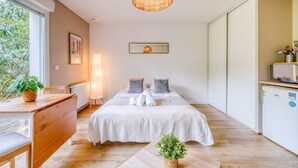 A bedroom with a bed, bedside table, lamp, and a view of the outdoors. - Jardins de Flore - Studio Apartment, Sleeps 2 (Mérignac)