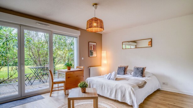 A bedroom with a bed, bedside table, and a view of the outdoors. - Jardins de Flore - Studio Apartment, Sleeps 2 (Mérignac)