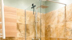 Une douche avec une porte en verre, des toilettes blanches et des carreaux de couleur beige.
