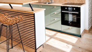 Une cuisine moderne avec des meubles de couleur verte, une cuisinière noire et un coin repas en bois.
