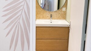 Une salle de bain avec un miroir rond, un lavabo blanc, un meuble-lavabo en bois et des carreaux de couleur beige.