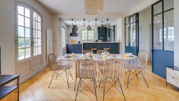 Een moderne keuken met een ronde eettafel, rieten stoelen en hanglampen.