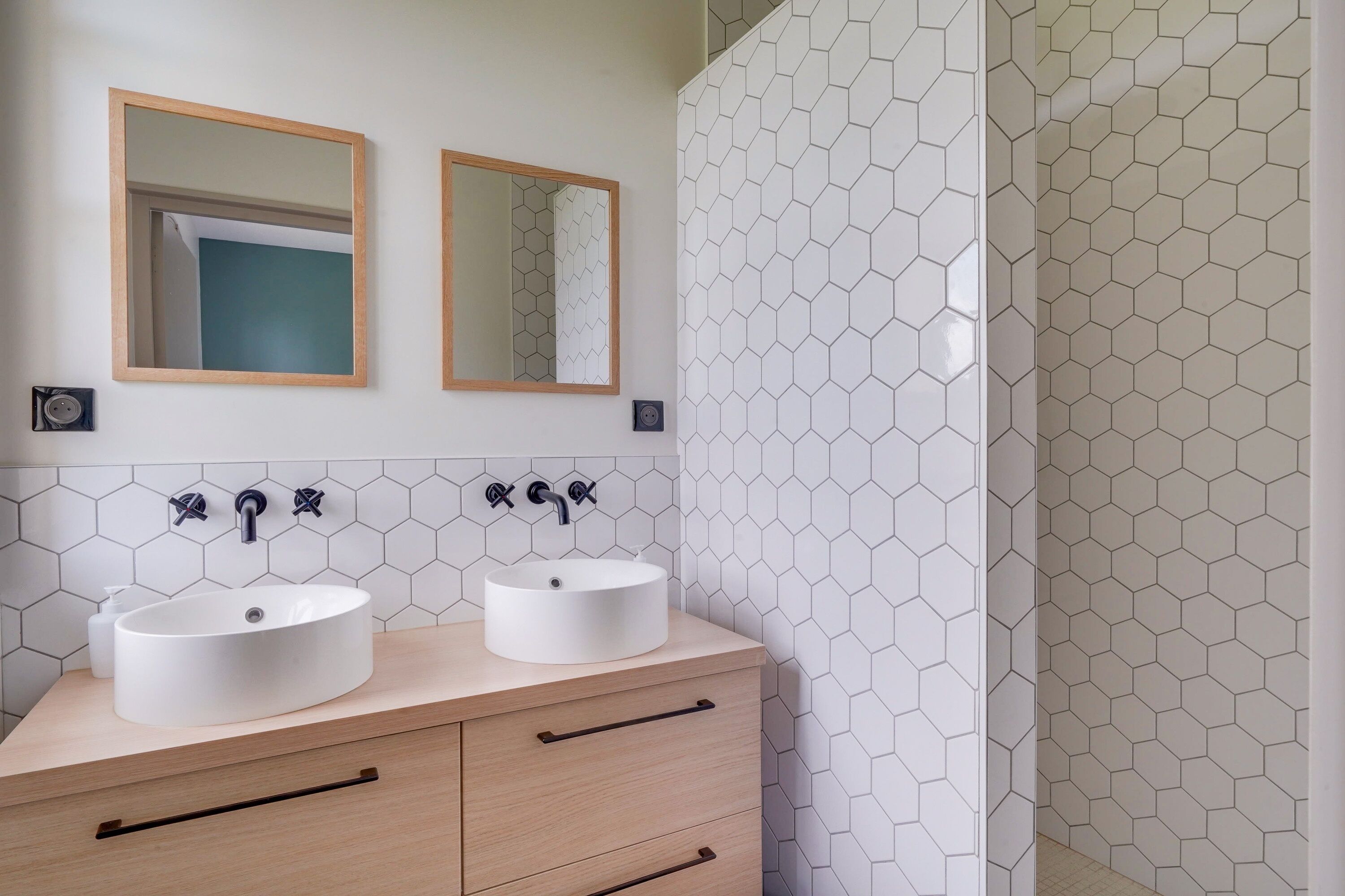 Casa de banho com duas pias, um espelho e um chuveiro com azulejos hexagonais nas paredes.
