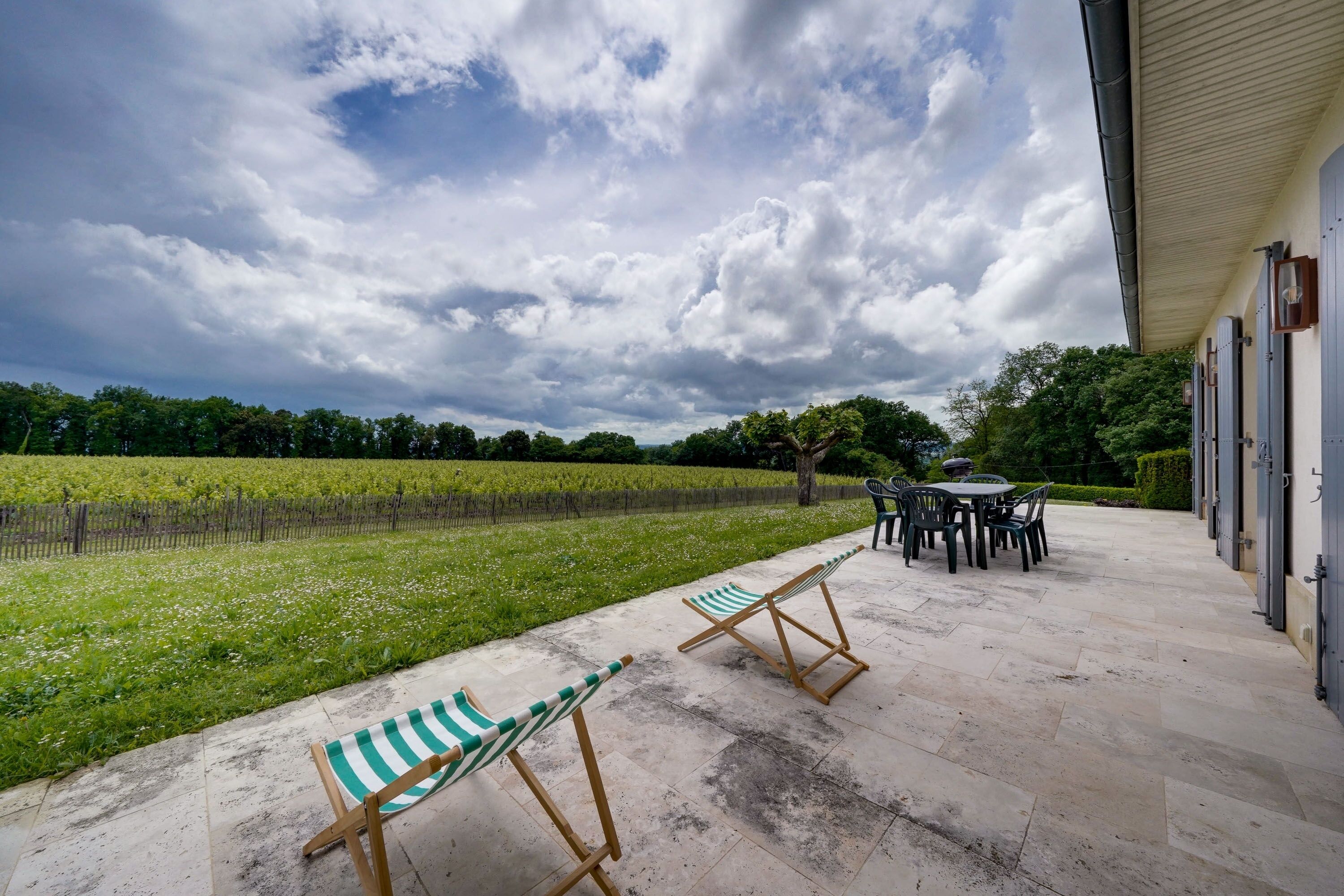 A patio with outdoor seating, a vineyard in the background, and a building with a covered walkway.