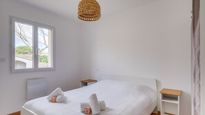 A bedroom with a bed, a bedside table, a hanging light fixture, and a window.
