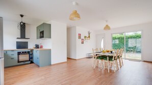 A modern kitchen with a built-in oven, microwave, and green cabinets. There is a dining area with a table and chairs, and a large sliding glass door leading to a garden.