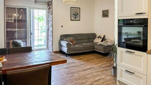 Ein Wohnzimmer mit Sofa, Esstisch und Küchenzeile mit Backofen.