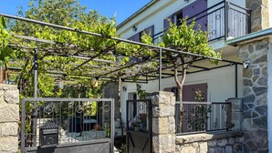 Ein Steinhaus mit einem Metallgitter, einer mit Wein bewachsenen Pergola und blauem Himmel.