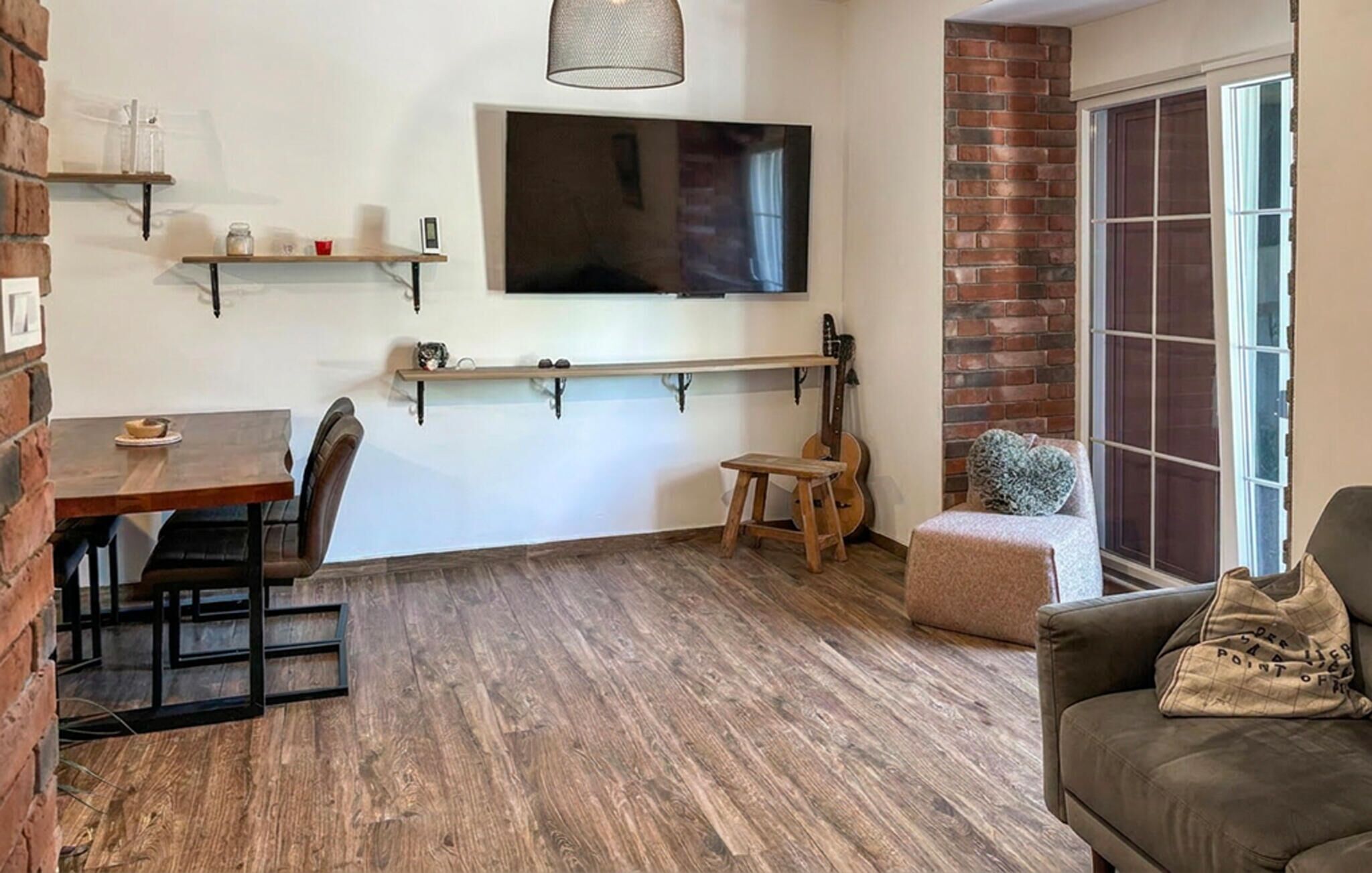 Un salon avec un téléviseur fixé au mur, une guitare, une petite table avec une chaise et un canapé.
