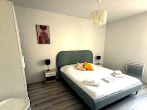 A modern bedroom with a bed, bedside tables, a nightstand, a wall-mounted lamp, and a radiator.