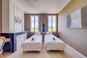 Habitación de hotel con dos camas, un escritorio, una silla, un ventanal grande y un cuadro en la pared.