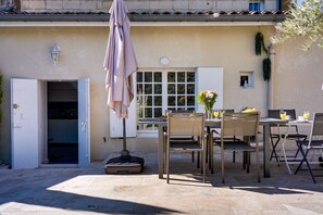 Un patio al aire libre con una mesa dispuesta para dos personas, una maleta y una sombrilla colgante.