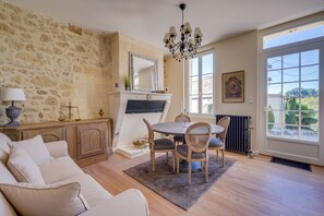 A room with a stone wall, a fireplace, a dining table with chairs, a sofa, and a large window. - Gîte des Coteaux - Three Bedroom House, Sleeps 6 (Fronsac)
