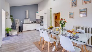 Een moderne keuken met witte kasten, een centraal kookeiland en een eethoek met een glazen tafel en witte stoelen.