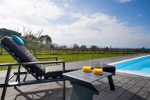 A poolside area with a lounge chair, a table with two glasses of orange juice, and a clear view of the pool and surrounding landscape. - Villa Héloïse - Three Bedroom House, Sleeps 6 (Camblanes-et-Meynac)