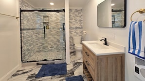 Un baño moderno con ducha de vidrio, lavamanos blanco y tocador de madera.