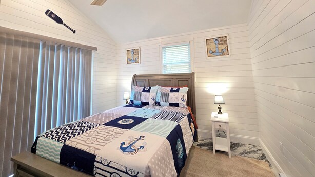 Un dormitorio con cama, ventilador de techo, mesita de noche con lámpara y decoración náutica.