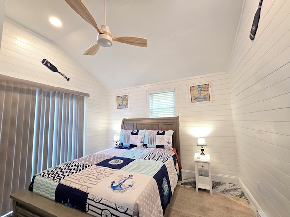 Un dormitorio con cama, ventilador de techo, mesita de noche con lámpara y decoración náutica.