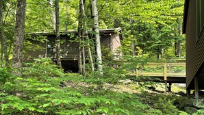 Una cabaña rústica rodeada de un bosque denso, una terraza de madera y un puente.