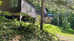 Una casa con porche cubierto y terraza, rodeada de un bosque frondoso.