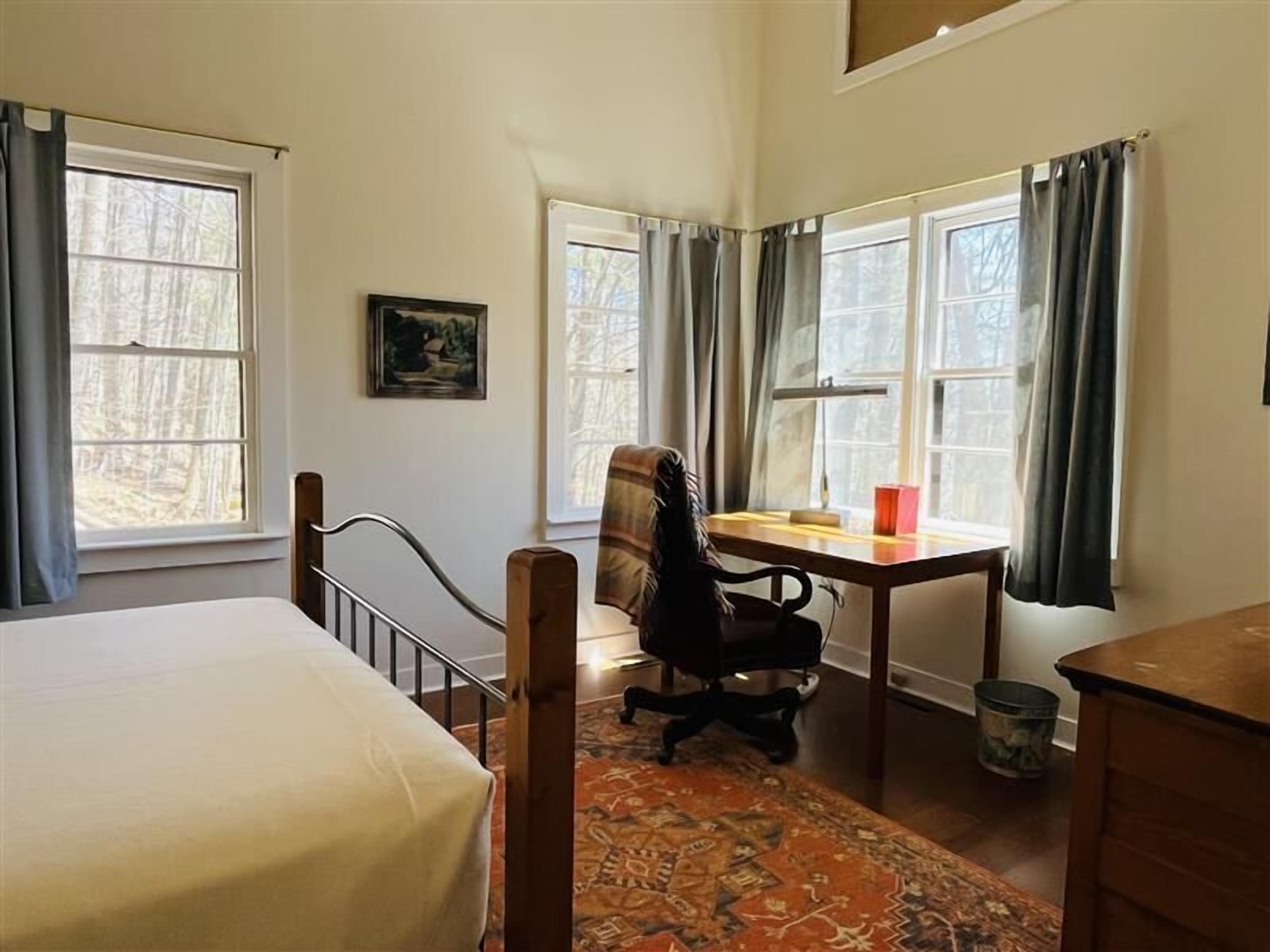 Un dormitorio con cama, escritorio, silla y alfombra.