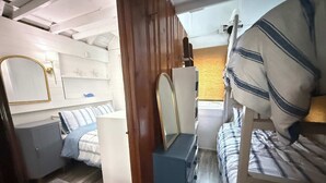 Ein kleines Schlafzimmer mit Etagenbett, Kommode, Spiegel und kleinem Fenster.