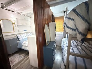 Ein kleines Schlafzimmer mit Etagenbett, Kommode, Spiegel und kleinem Fenster.