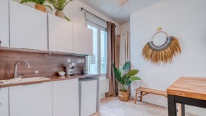 A modern kitchen with white cabinets, a wooden countertop, a sink, a small refrigerator, and a dining area with a table and bench.