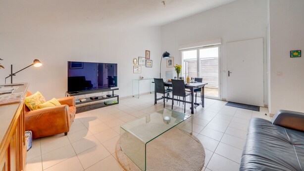 A modern living room with a flat-screen TV, leather sofas, a glass coffee table, and a dining area with chairs and a table.