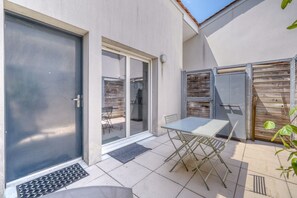 Une terrasse avec une table et des chaises, une porte-fenêtre coulissante et un petit jardin.