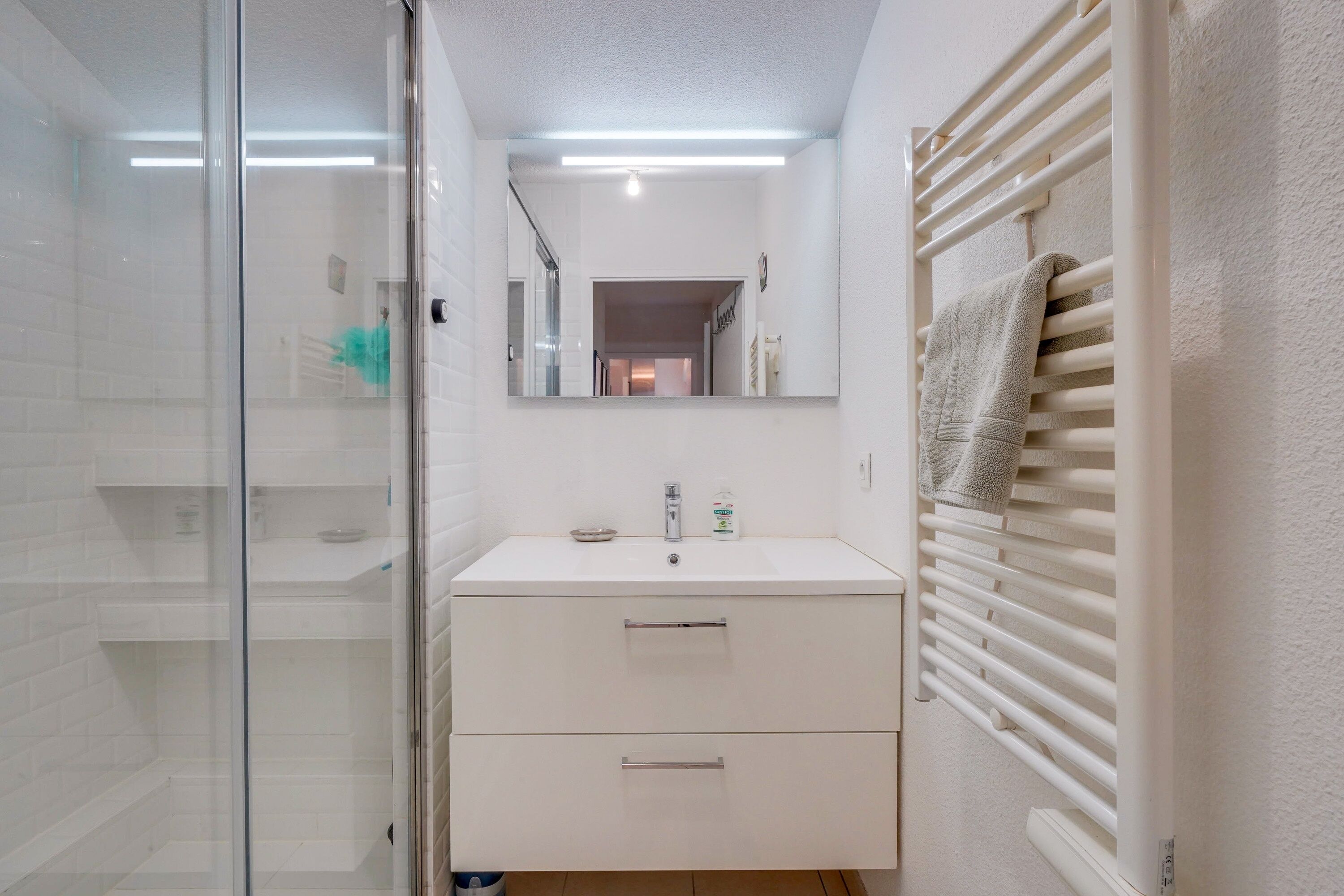 A modern bathroom with a glass shower enclosure, a white sink with a mirror above it, and a towel rack on the wall.