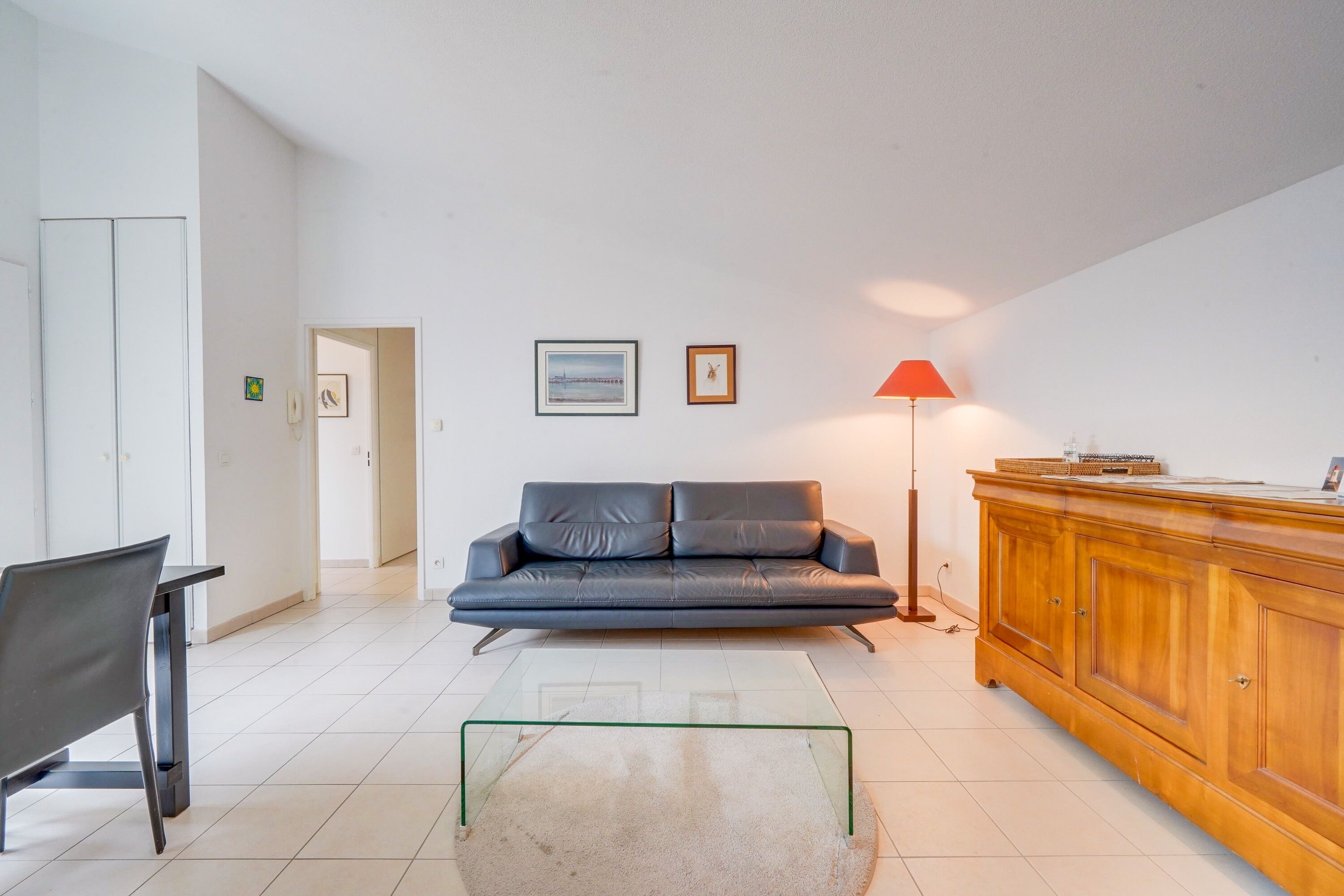 A modern living room with a sofa, a glass coffee table, a wooden cabinet, and a red floor lamp.