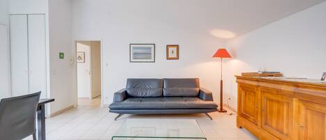 A modern living room with a sofa, a glass coffee table, a wooden cabinet, and a red floor lamp.