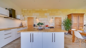 Een moderne keuken met witte kasten, een groot eiland, een stenen muur, houten kasten en een eetgedeelte met een tafel en stoelen.