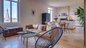 Een moderne woonkamer met een bank, stoelen, een eettafel en een keukenhoek met kasten en een magnetron.