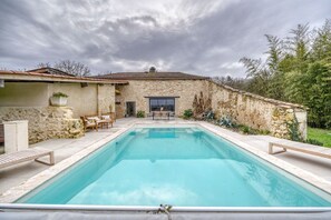 Una piscina rettangolare con una parete in pietra e un'uscita verso un patio.