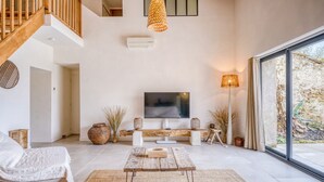 Una sala de estar moderna con televisor, mesa de centro de madera y un ventanal grande.