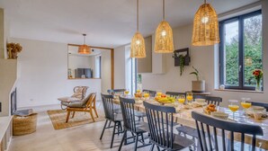 Un comedor con una mesa larga, sillas, lámparas de mimbre colgantes y un ventanal con vistas a la vegetación.