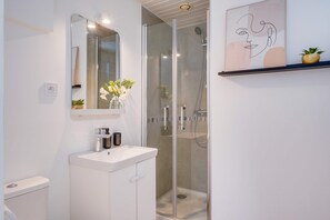 Une salle de bain moderne avec une douche Ă parois de verre, un lavabo blanc et une dĂ©coration minimaliste comprenant un vase avec des fleurs et une Ćuvre dâart murale.