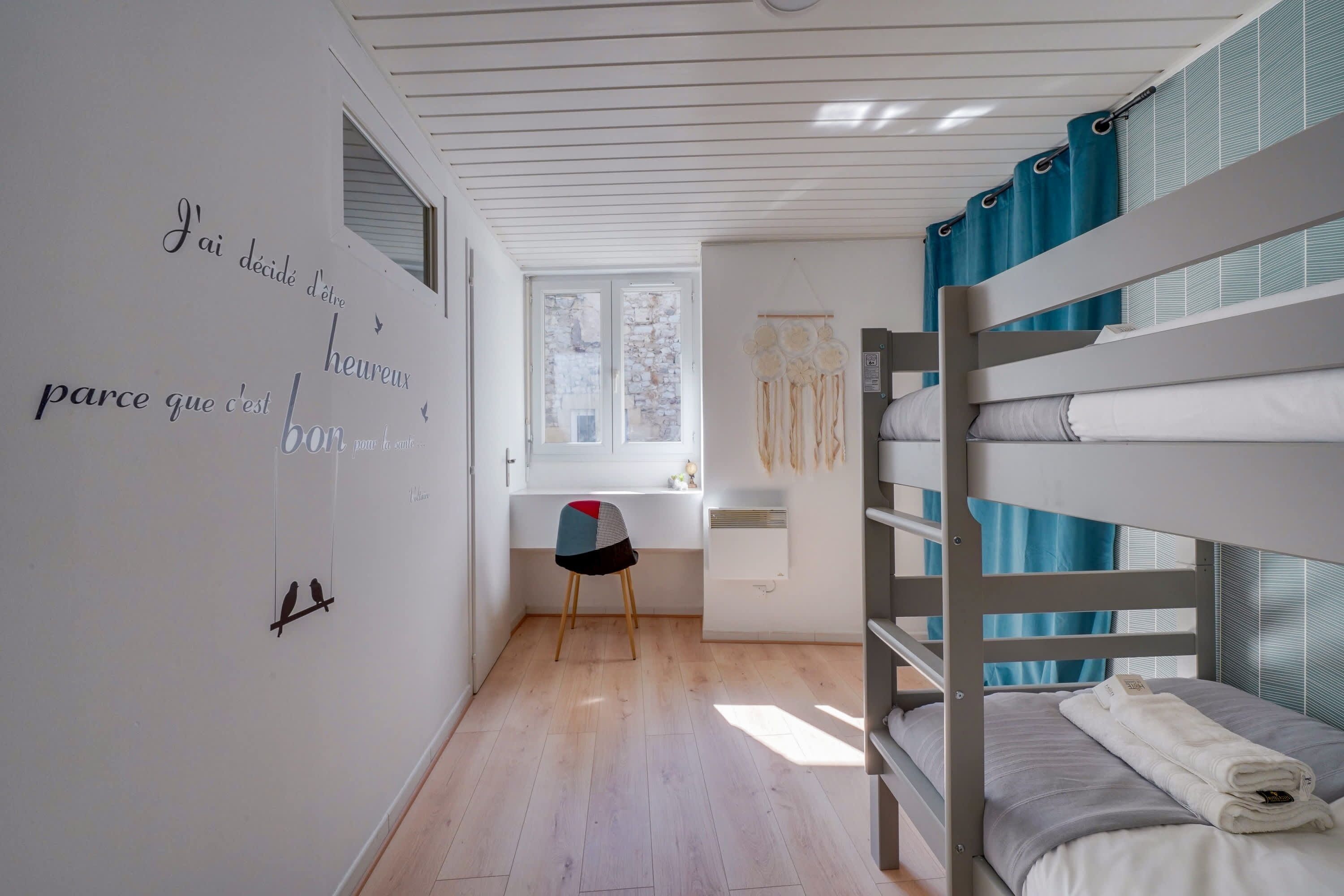 Habitación con literas, ventana, una silla y pared con texto e ilustraciones de pájaros.